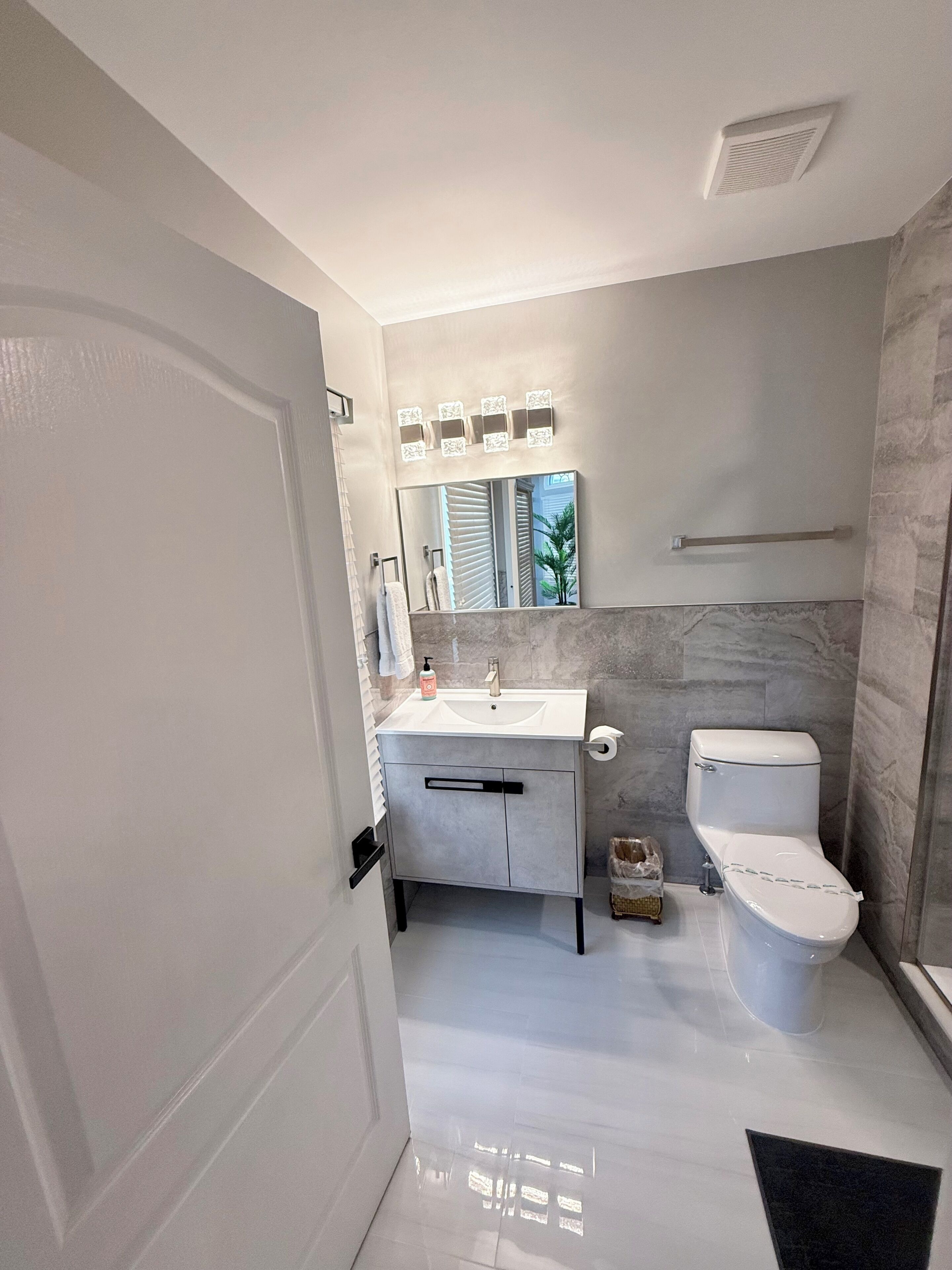 Un baño moderno con lavamanos, espejo y retrete blancos.