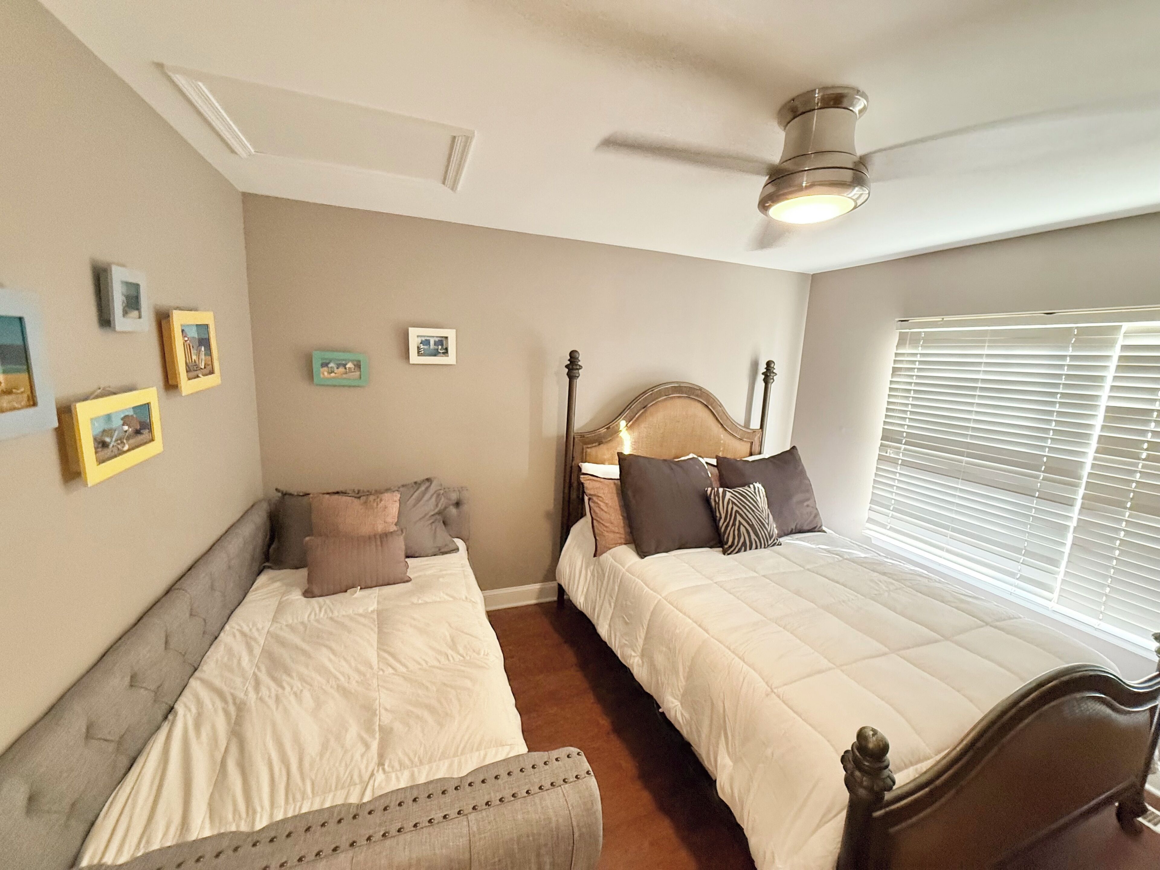 A bedroom with two beds, a ceiling fan, and a window with blinds.