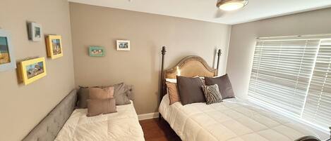 A bedroom with two beds, a ceiling fan, and a window with blinds.