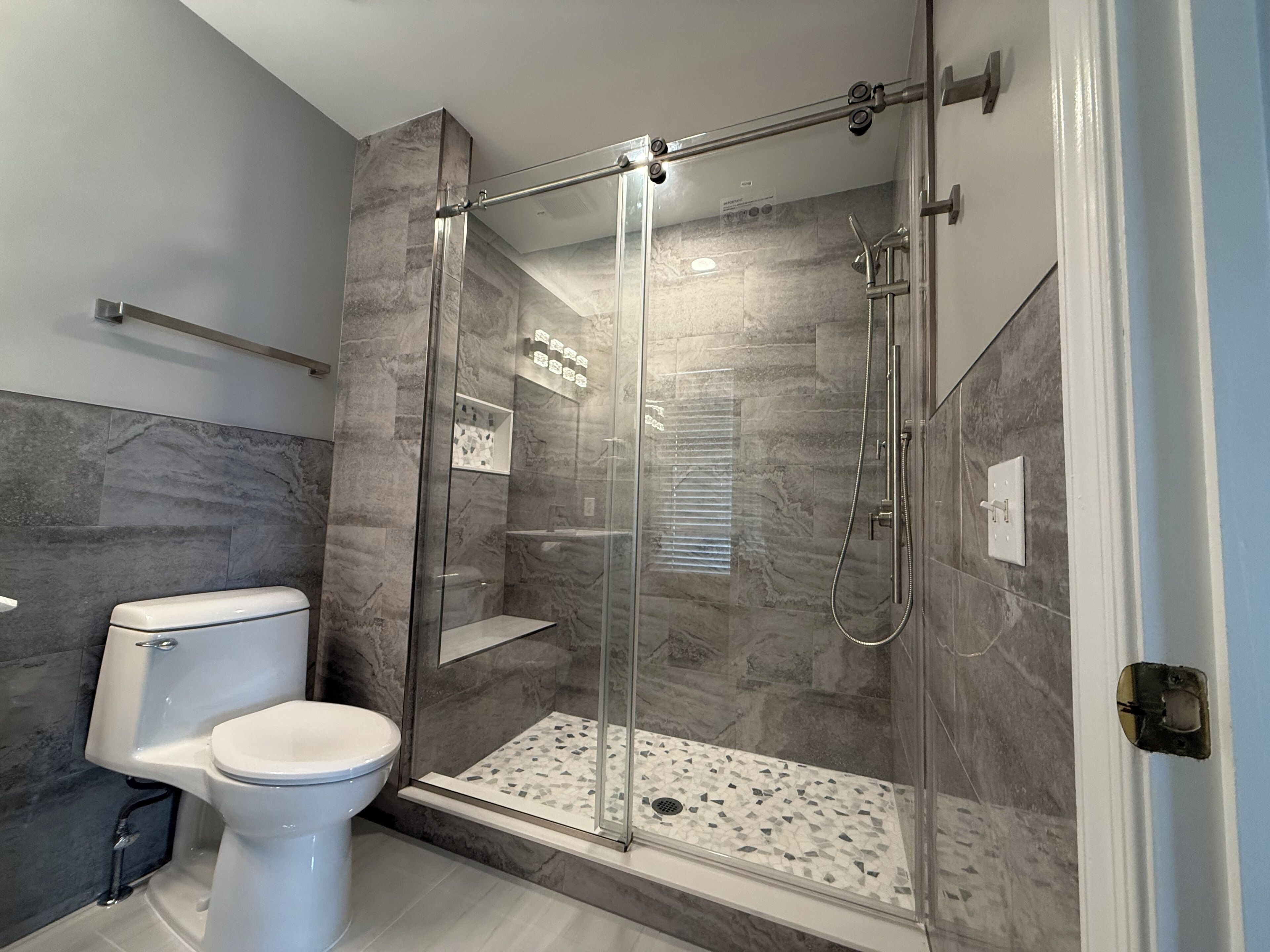A modern bathroom with a glass-enclosed shower, a toilet, and a marble backsplash.