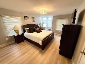 Een slaapkamer met een groot bed, nachtkastje, lamp, dressoir en televisie.
