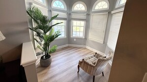 A room with a large potted plant, a striped armchair, and multiple arched windows.