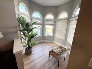 Une pièce avec une grande plante en pot, un fauteuil à rayures et plusieurs fenêtres en arc de cercle.