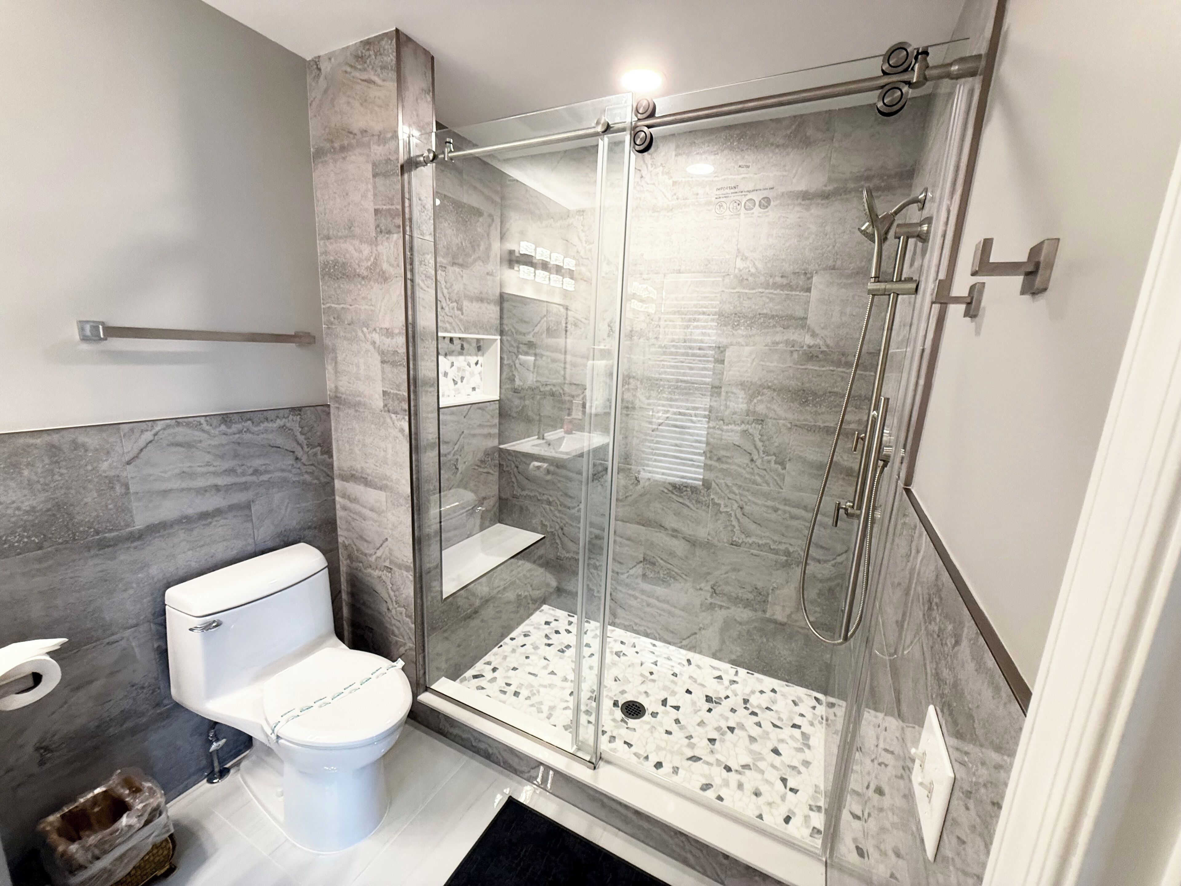 A modern bathroom with a glass-enclosed shower, a toilet, and a marble-tiled floor.