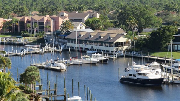 A marina with multiple boats docked, a building with a sloped roof, and surrounding greenery.