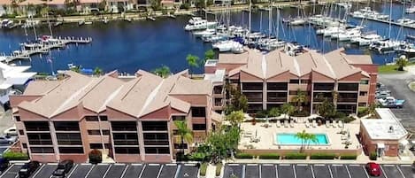 A marina with multiple boats, a hotel with a pool, and a parking lot.