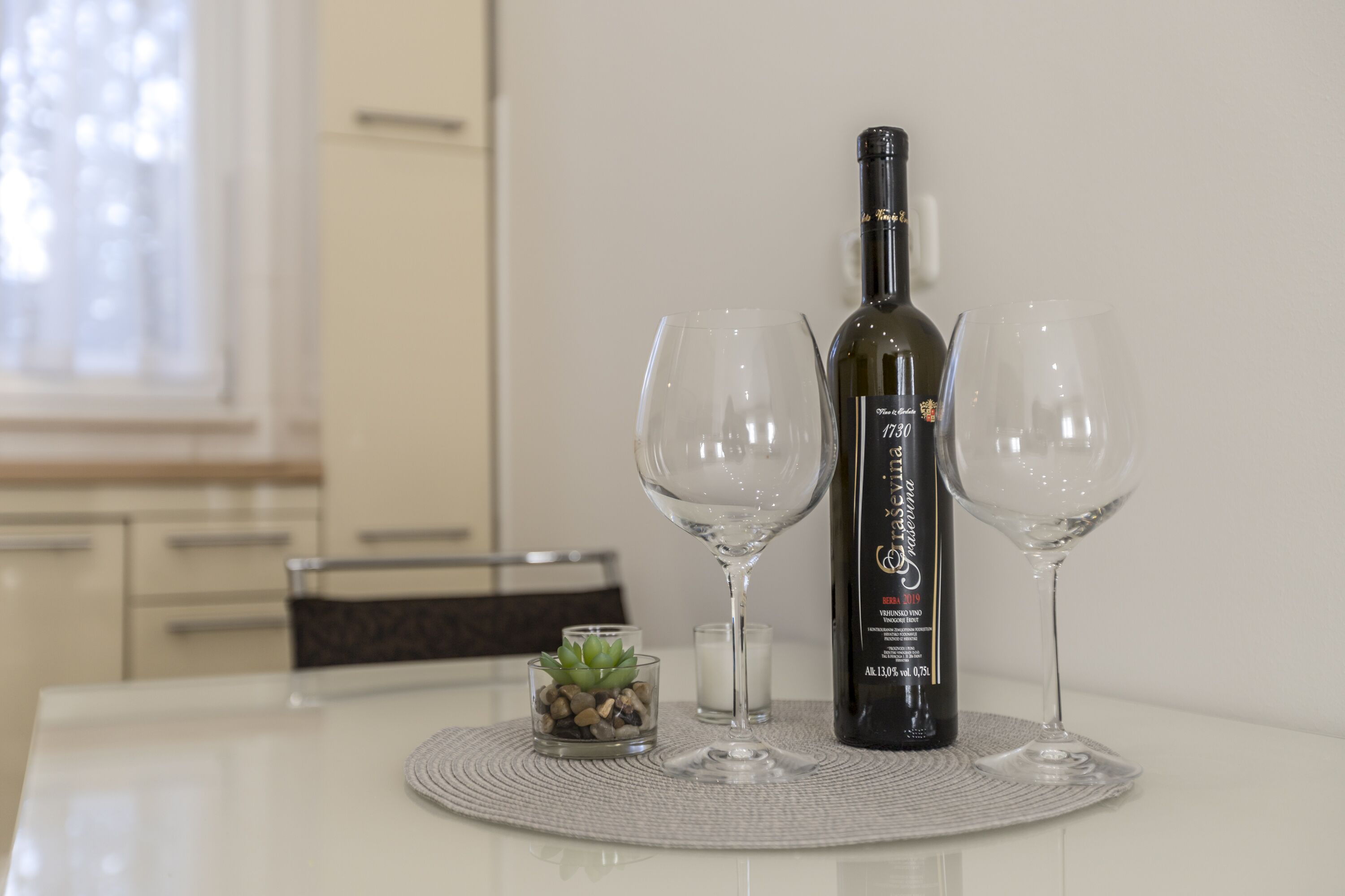 A bottle of wine on a table with two glasses and a small plant.