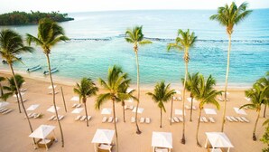 A beach with rows of palm trees and beach chairs, a boat in the water, and a clear view of the ocean. - Beautiful sea view Golf Villa in Casa de Campo (La Romana)
