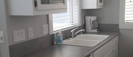 Una cocina con armarios blancos, un lavamanos doble y una ventana con persianas.