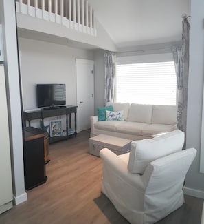 Uma sala de estar com um sofá branco, uma televisão e uma mesinha com objetos decorativos.