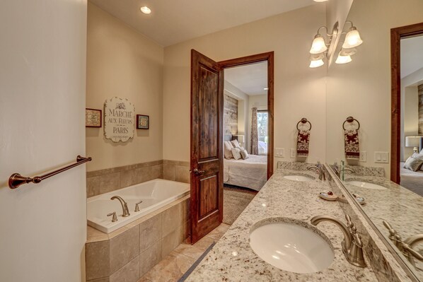 A bathroom with a double sink, a bathtub, and a large mirror.