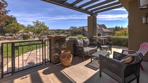 An outdoor patio with wicker furniture, a stone wall, and a view of a residential neighborhood.