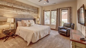 A bedroom with a large bed, a desk, a chair, a ceiling fan, and a window with curtains.