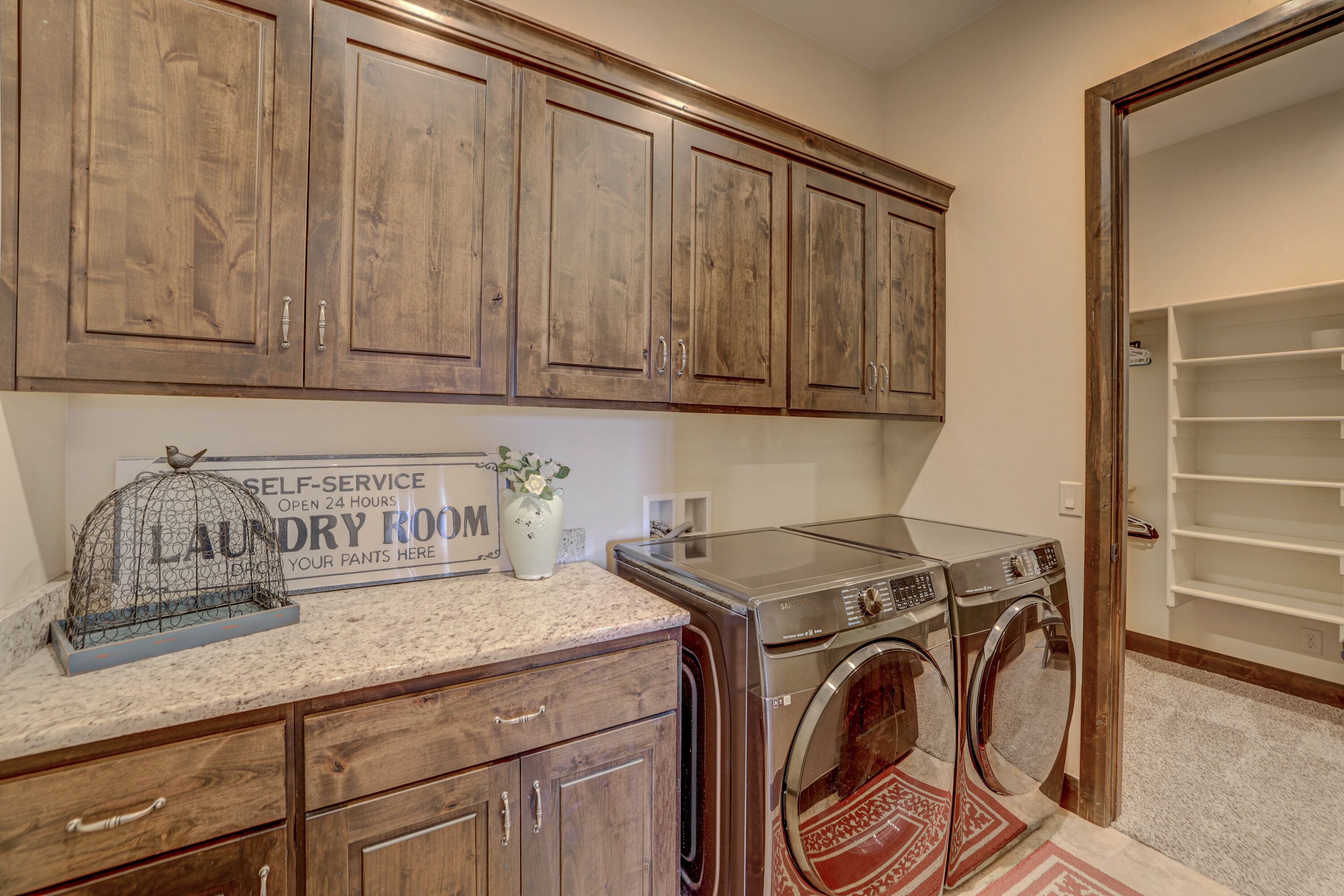A laundry room with wooden cabinets, a self-service sign, and two stacked front-loading washers.
