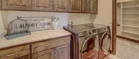 A laundry room with wooden cabinets, a self-service sign, and two stacked front-loading washers.