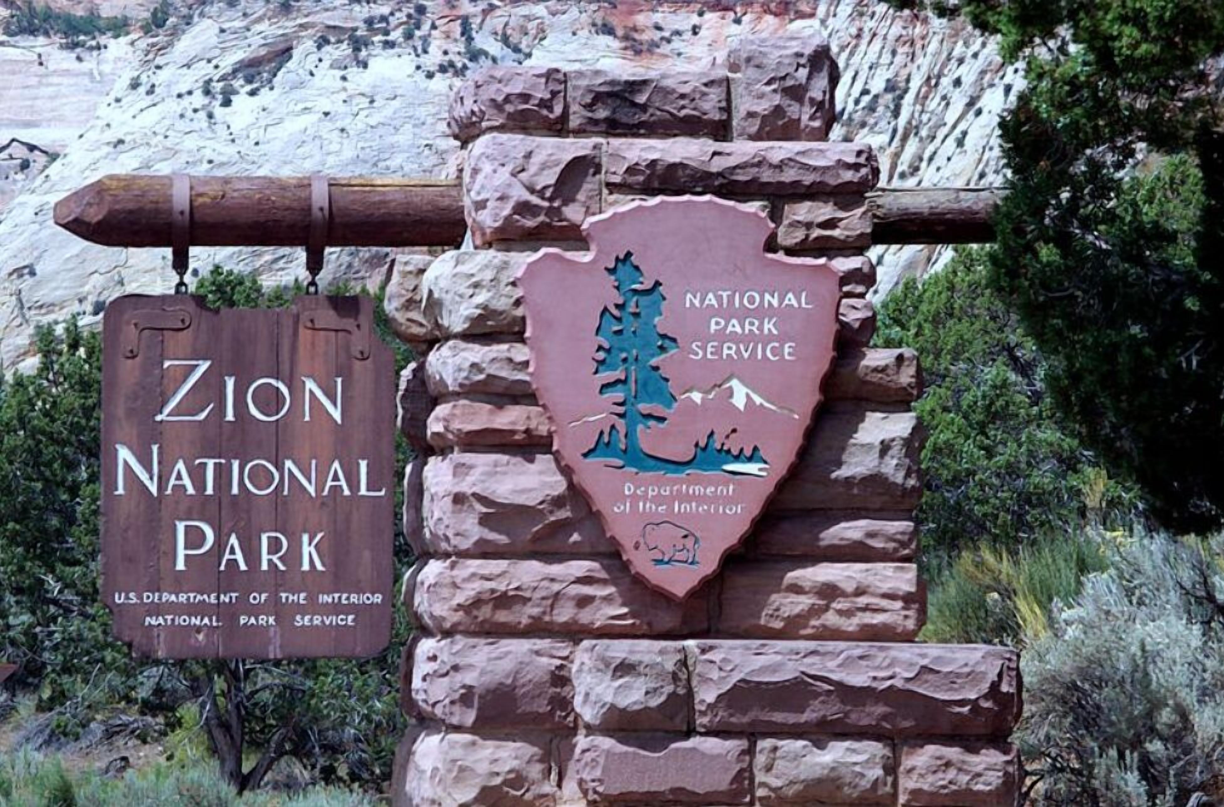 A wooden sign for Zion National Park and a stone sign for the National Park Service.