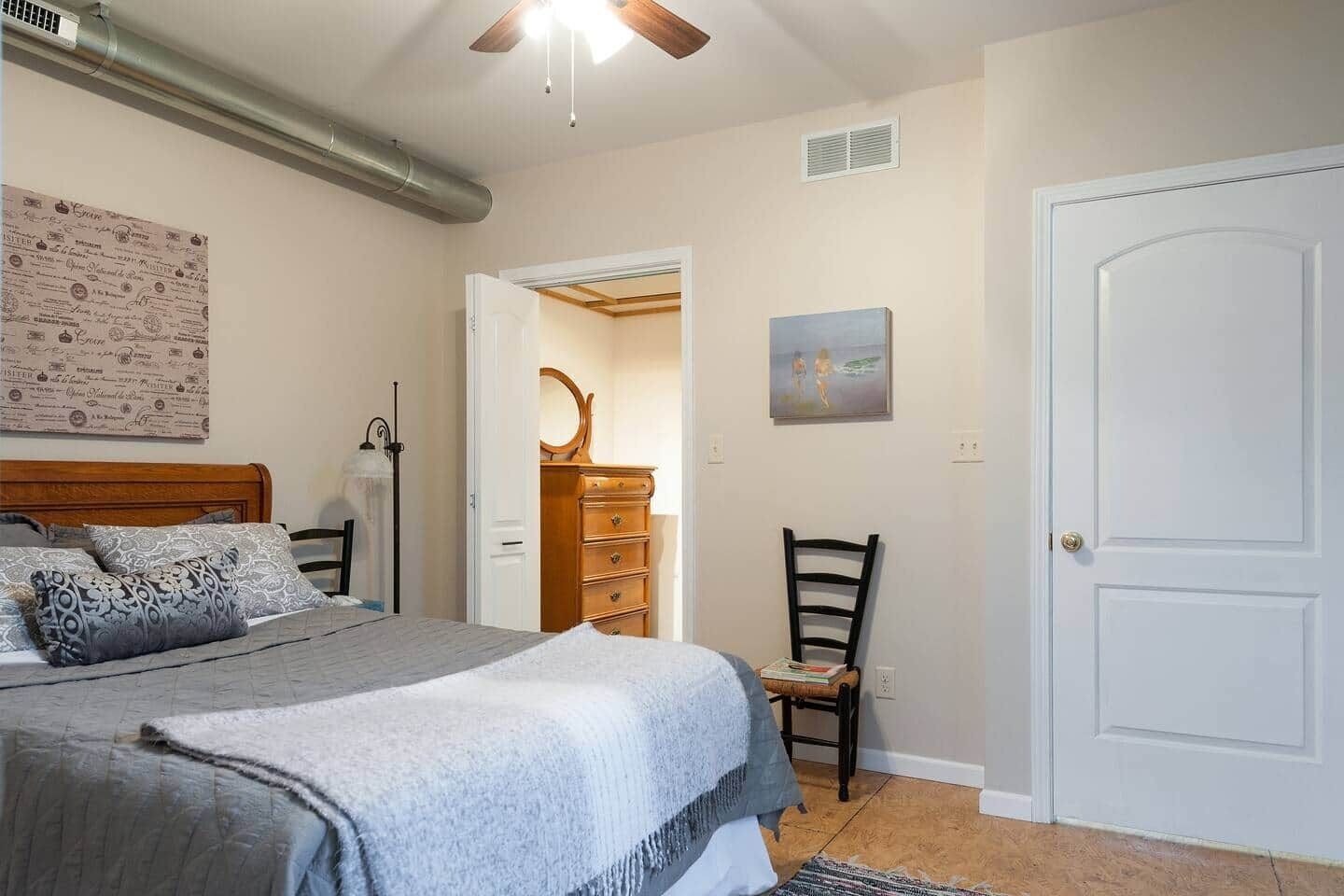 A bedroom with a bed, dresser, chair, and a door.
