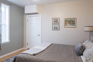A bedroom with a bed, a window, a door, and two framed pictures on the wall.