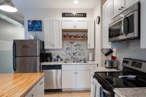 A modern kitchen with white cabinets, a stainless steel refrigerator, a microwave, an oven, and a coffee maker. - We do Italian STL style. Perfecto! Enjoy our NBHD! (St. Louis)