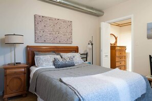 A bedroom with a bed, bedside tables, a lamp, a dresser, and a door leading to another room. - We do Italian STL style. Perfecto! Enjoy our NBHD! (St. Louis)