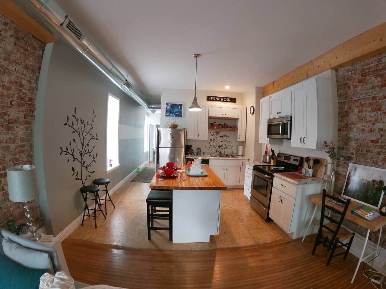 A modern kitchen with a central island, white cabinetry, and a brick accent wall.