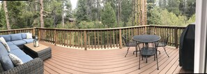 Relax on the deck surrounded by a dense forest, with a sofa set and table for a peaceful retreat.