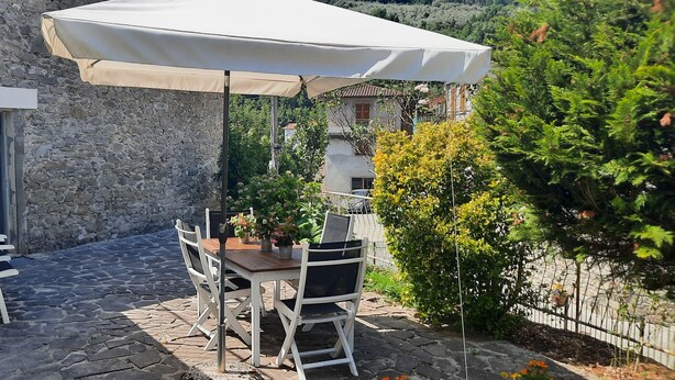 A stone building with a patio area featuring a table and chairs under a canopy, surrounded by greenery and a stone wall. - The Haven of Angels (MASSA)