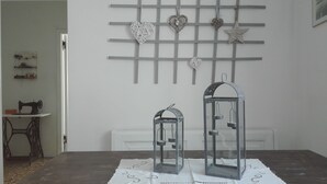 A room with a table displaying two lanterns, a sewing machine, and a wall with decorative items. - The Haven of Angels (MASSA)