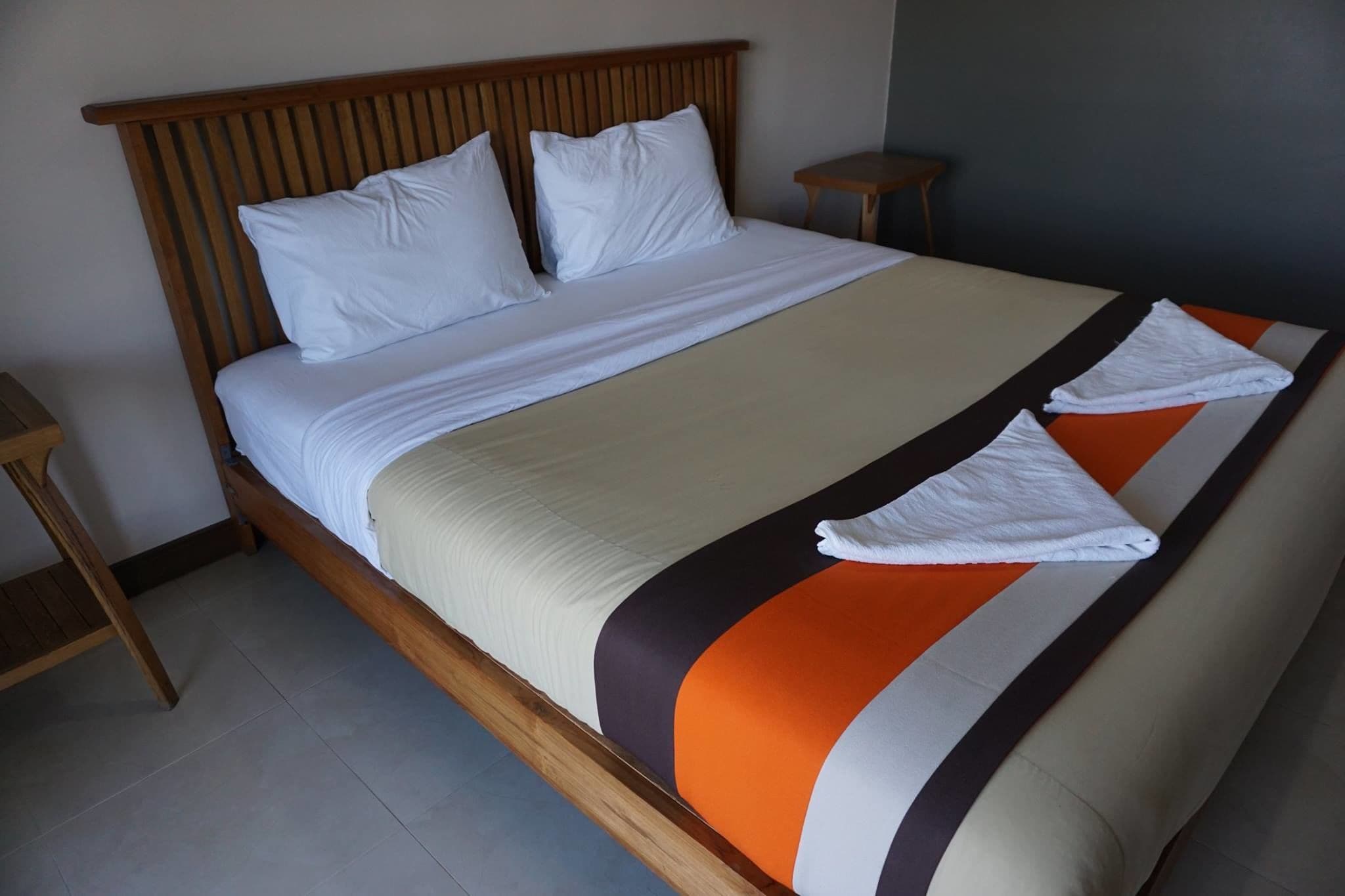 Una cama bien tendida con sábanas blancas y una colcha a rayas, un cabecero de madera y dos mesitas de noche.
