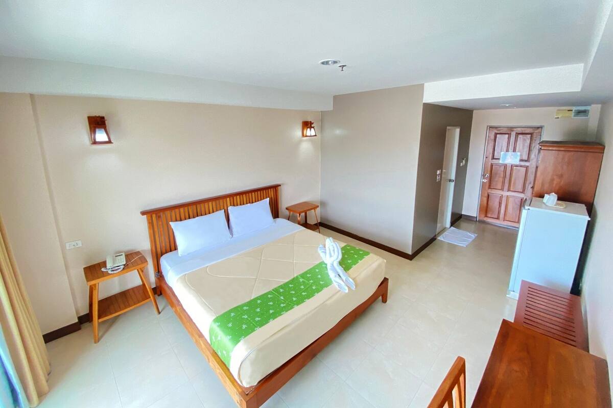 A hotel room with a bed, bedside tables, a desk, a wardrobe, and a door leading to another room.