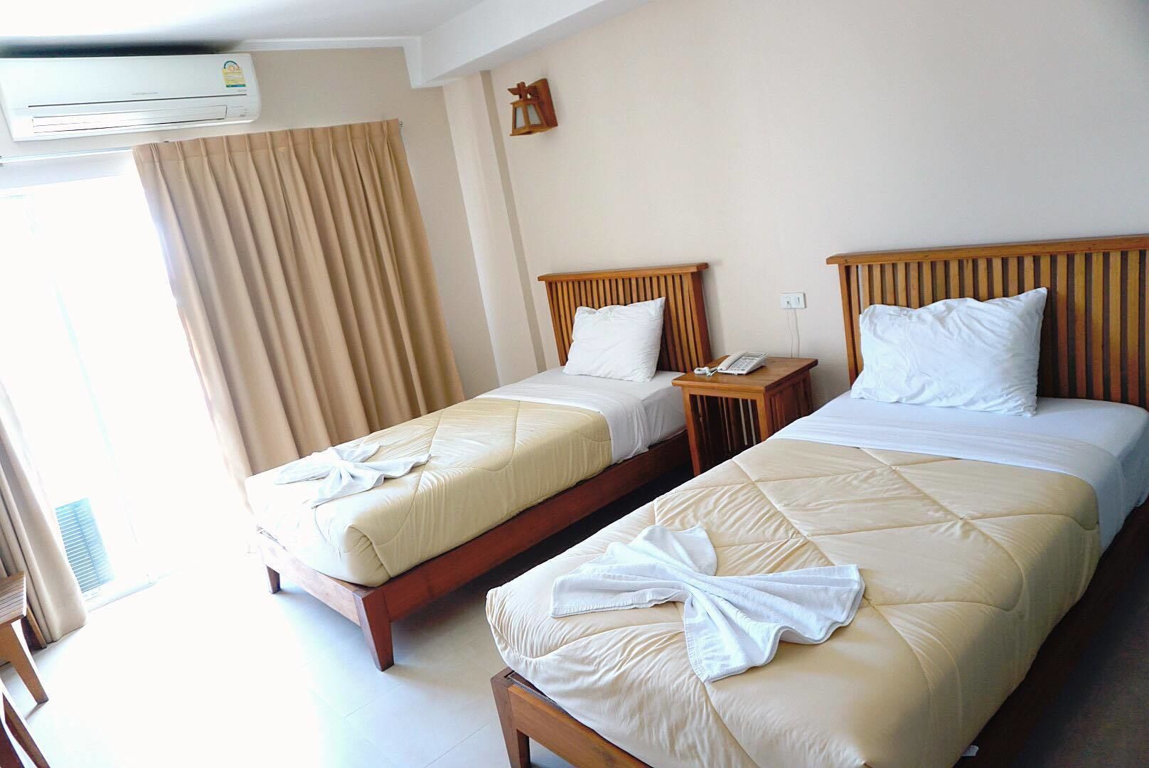 Een hotelkamer met twee bedden, een houten hoofdbord, een nachtkastje met een telefoon en een airconditioning.