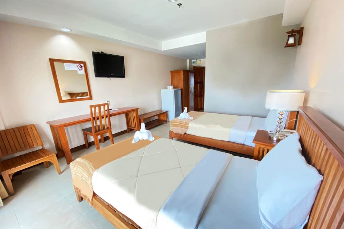A hotel room with two beds, a desk, a chair, a television, and a lamp.