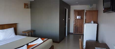 A hotel room with a bed, a small table, a refrigerator, and a television.