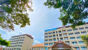 A multi-story hotel with a central entrance, a parking area, and a clear sky. - Maihom Resort Dechatiwong Bridge (Nakhon Sawan)