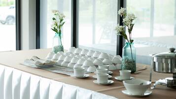 A table with white teacups and saucers, a teapot, and two vases with flowers.