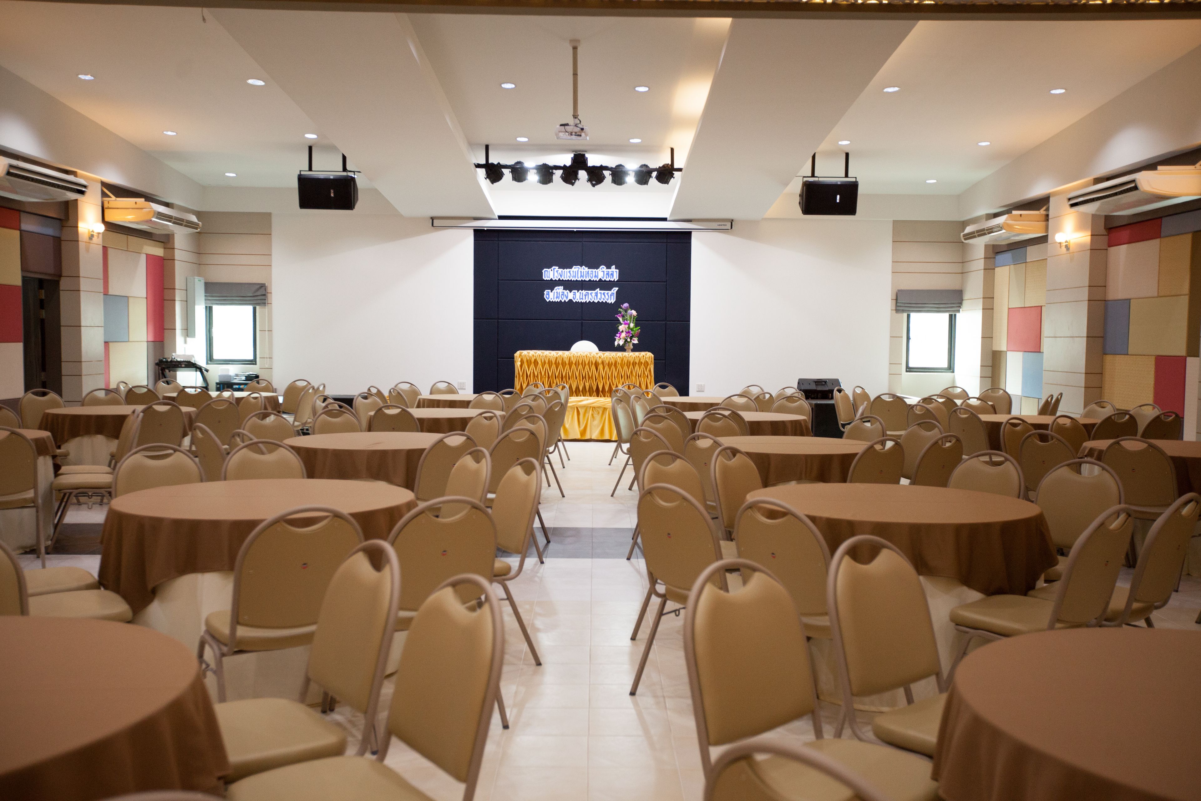 A conference room with round tables and chairs, a stage with a projector, and a large screen displaying text.