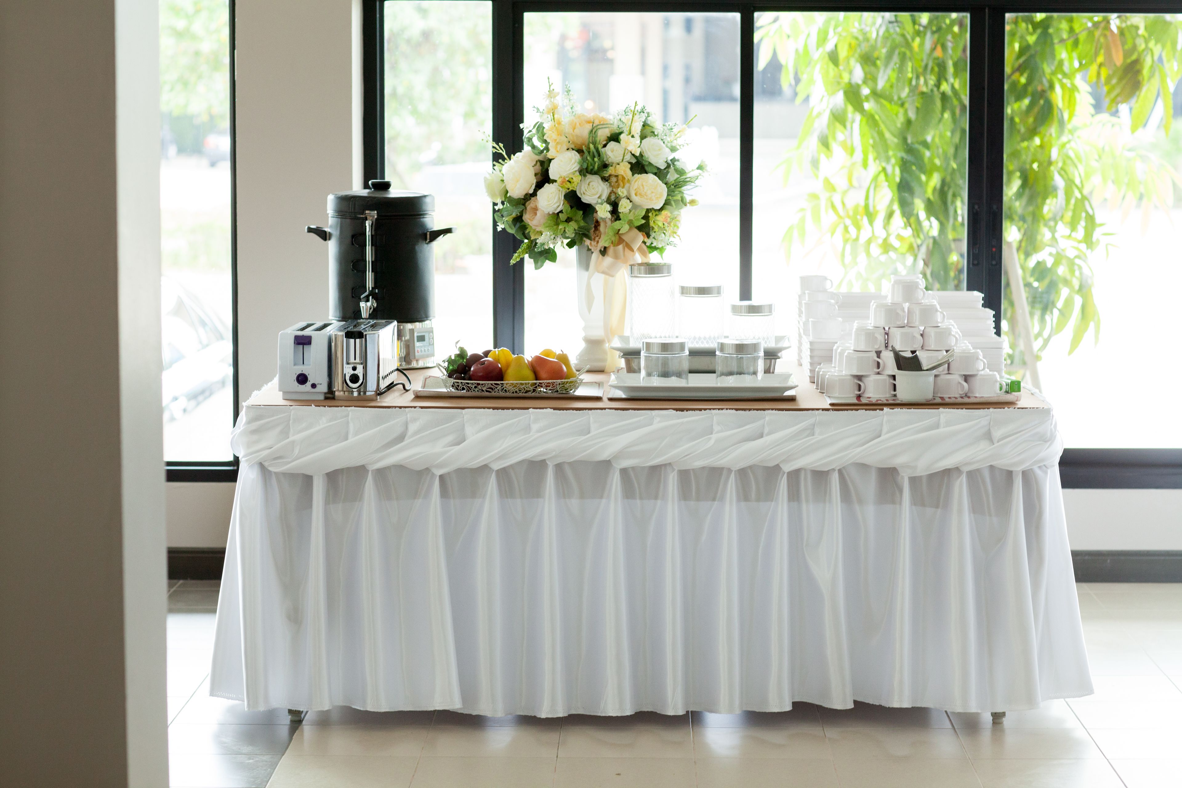 A table with a coffee maker, a bowl of fruit, and a vase of flowers.