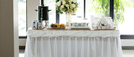 A table with a coffee maker, a bowl of fruit, and a vase of flowers.