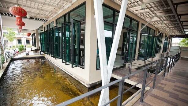 A modern building with a long corridor, large windows, and a water feature. - MaiHom Villa (Nakhon Sawan)