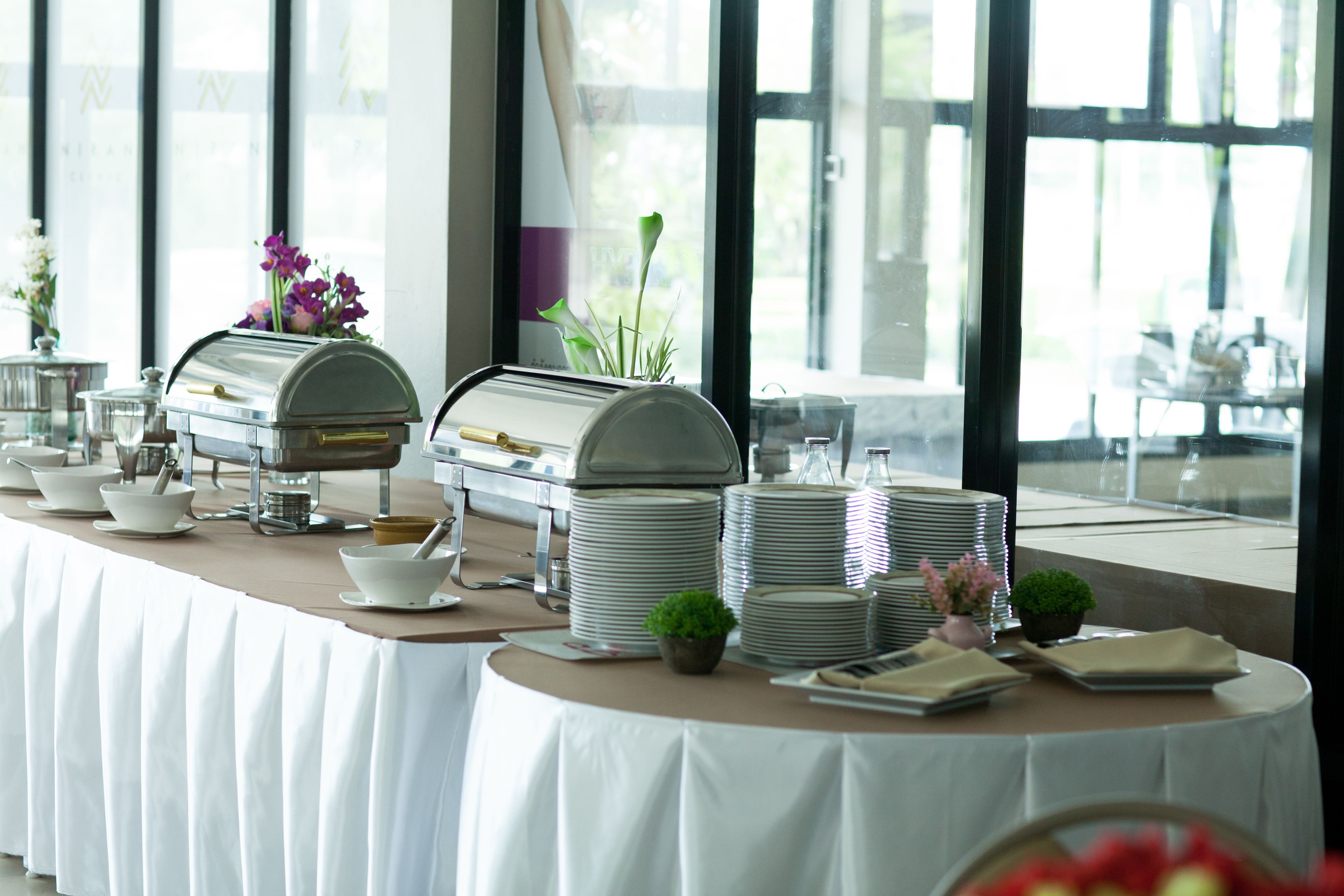 Disposição de buffet com várias estações de serviço, incluindo máquina de café, tigelas, pratos e pequenas plantas em vasos.