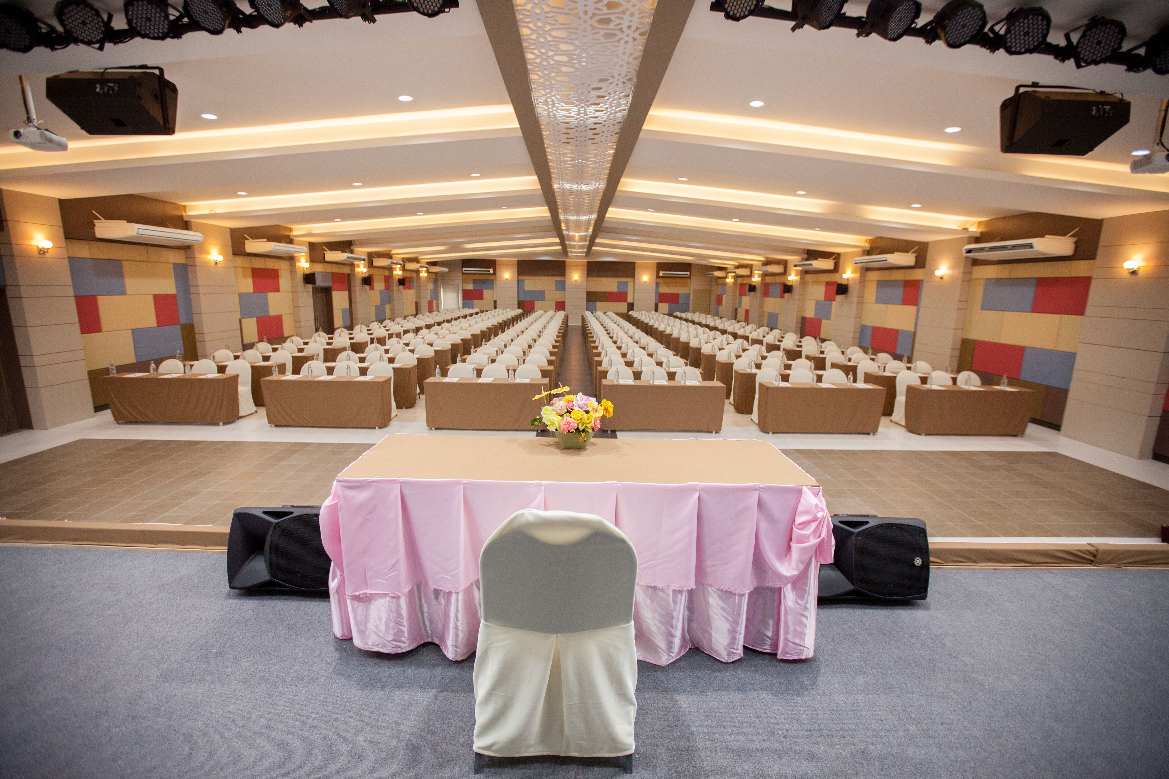 A conference room with rows of chairs, a long table with a pink tablecloth, and a floral centerpiece.
