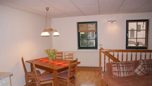 Un comedor con mesa y sillas de madera, un jarrón con flores y un banco de madera con cojines.
