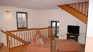 Un salón con escalera de madera, un sofá, un televisor y un ventanal con vistas al exterior.