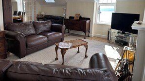 A living room with a brown leather sofa, a wooden coffee table, a television, and a fireplace. - Sealladh na Mara (Gaelic for "View of the Sea") (Isle of Arran)