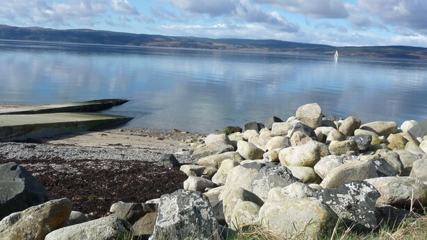 A calm lake with a rocky shoreline and a distant sailboat. - Sealladh na Mara (Gaelic for "View of the Sea") (Isle of Arran)