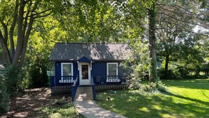 A small, single-story house with a dark blue exterior, a front porch with a bench, and a pathway leading to the entrance.