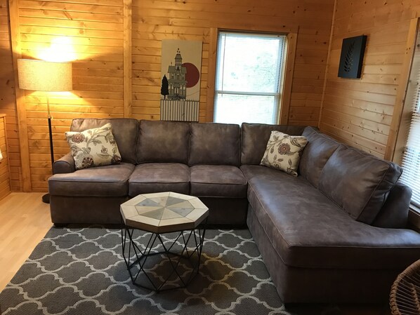 Interior acogedor de una cabaña de madera con un sofá de cuero marrón, una mesa de centro geométrica y almohadones estampados.