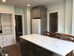 Una cocina con encimera de mármol blanco, armarios oscuros y un refrigerador.