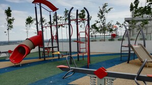 A playground with a red slide, swings, and a seesaw.