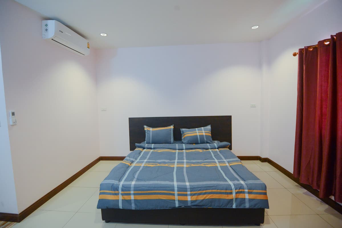 A bedroom with a bed, a headboard, a window, and a red curtain.
